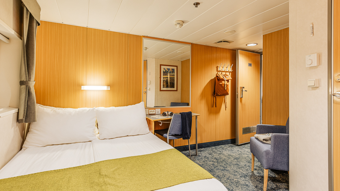 Double bed in white & green-colored linens by window, desk & blue chair in Double Cabin aboard Quest Arctic expedition ship.