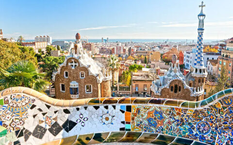 View from colorful tiled Park Guell overlook in Barcelona, Spain with brick & blue & white buildings below.