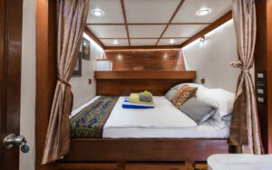Katharina sailboat stateroom with a double bed and upper shelf storage. Curtain and overhead lighting for the bed.