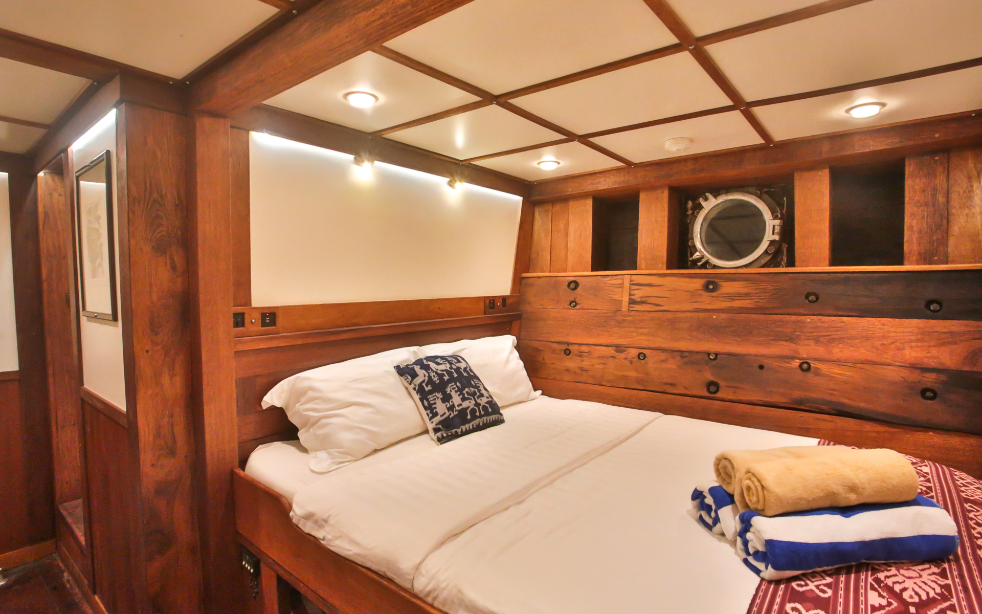 Double Cabin aboard small cruise Ombak Putih small ship. Room with wooden design on walls, overhead lighting, and towel display on bed