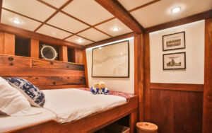 Double Cabin aboard small cruise Ombak Putih small ship. Room with wooden design on walls, overhead lighting, and towel display on bed