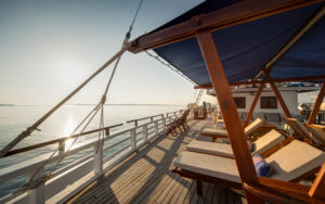 Deck aboard small ship Ombak Putih with several of lounge chairs under a royal blue canvas awning on a sunny afternoon on the water