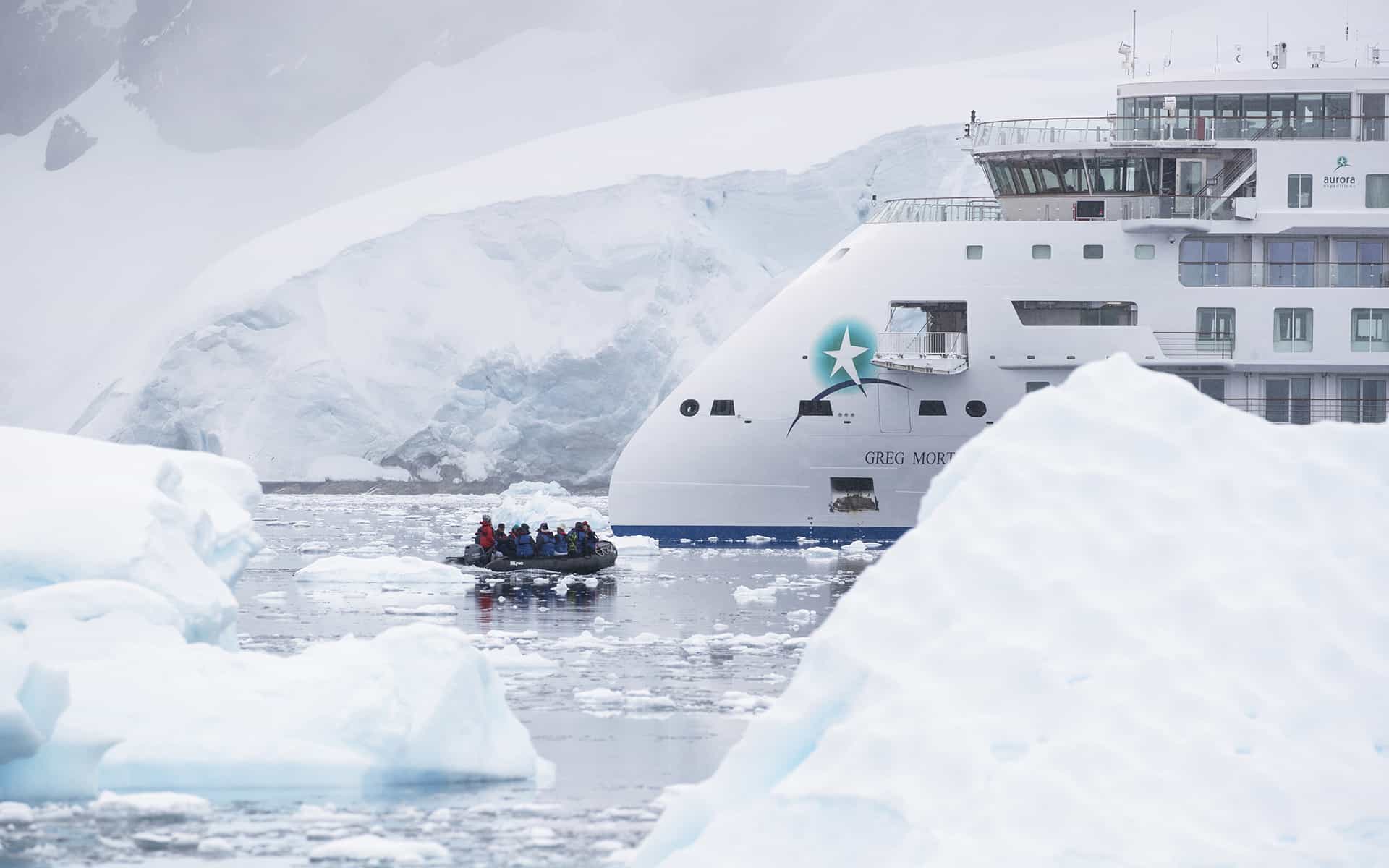 Antarctica travelers ride in a Zodiac through iceberg-filled, calm waters in front of a small white expedition ship.