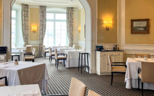 Restaurant in Casa Gangotena Hotel with white linen tables set for a meal. Floor-to-ceiling drapes frame large windows in background.