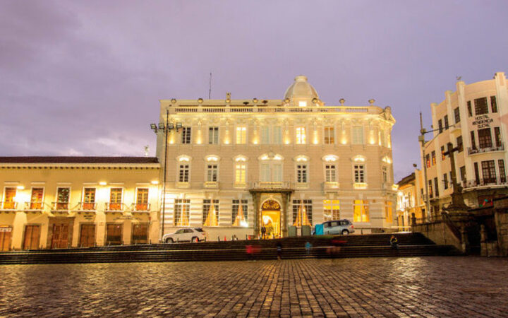Cobblestone street plaza in front of bright, well-lit Casa Gangotena hotel and historic mansion in Quito, Ecuador on a cloudy evening