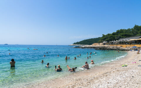 Group of people enjoying the Croatian waters on a beach with turquoise water on a sunny day. Green coast line wrapping around beach