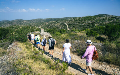 Group hiking on a sunny day during Dalmatian Coast & Ionian Sea small ship cruise. Rolling hills, zig zag road, and stone ruins in background