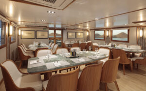 Spacious dining room aboard the small cruise ship Evolution. Tables are set for a meal and cushioned chairs line the edges.