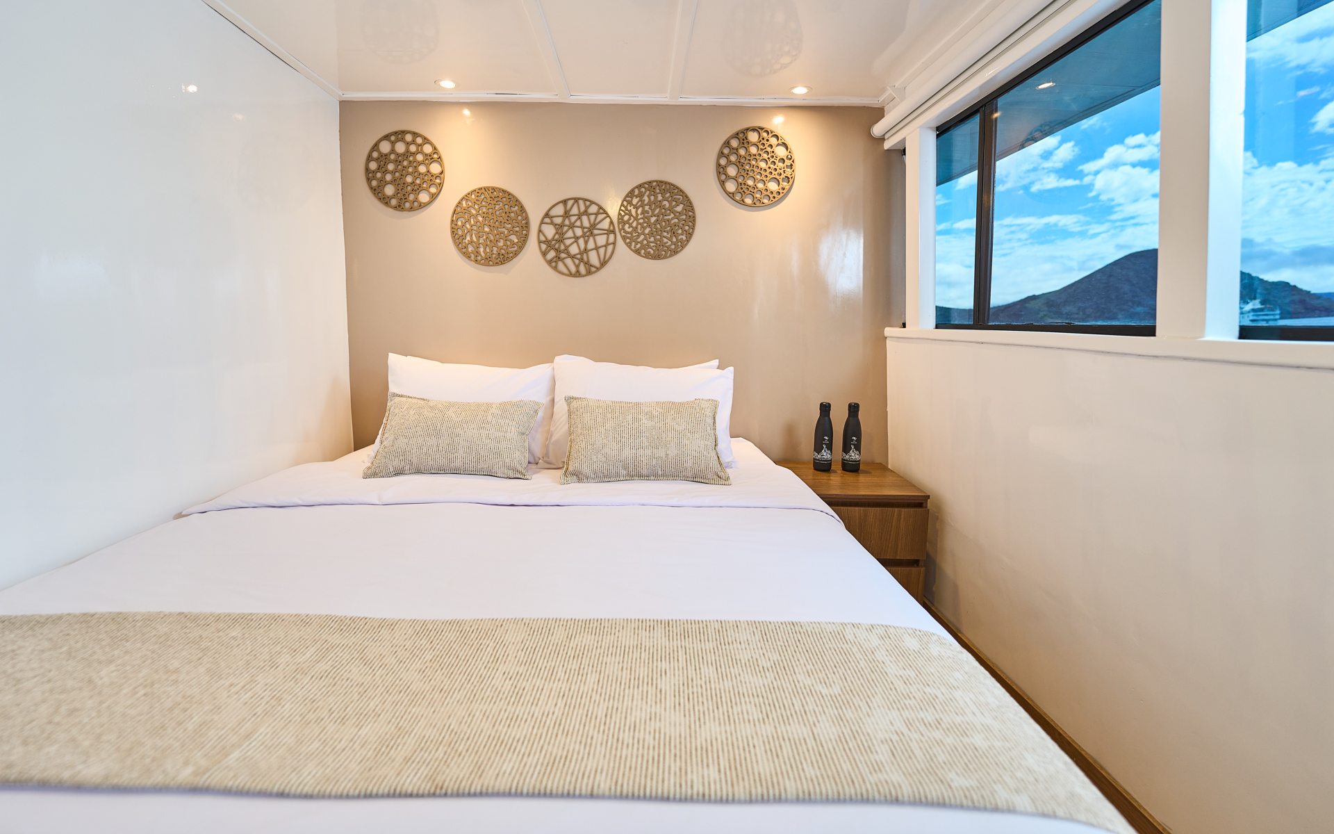 Upper Deck Cabin on Monserrat boat in Galapagos with matrimonial-size bed in white, beige accents & big view window.