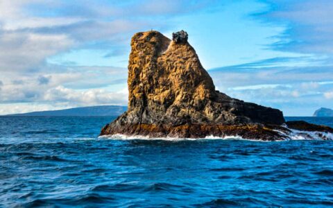 Pinnacle Rock juts above the ocean under the sky with clouds at the Galapagos Islands