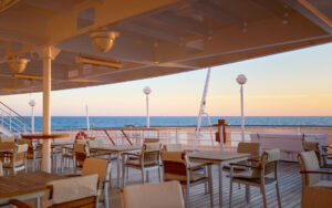 Spacious partly covered deck with several white 4-top tables during a clear-sky sunset aboard small ship Heritage Adventurer.