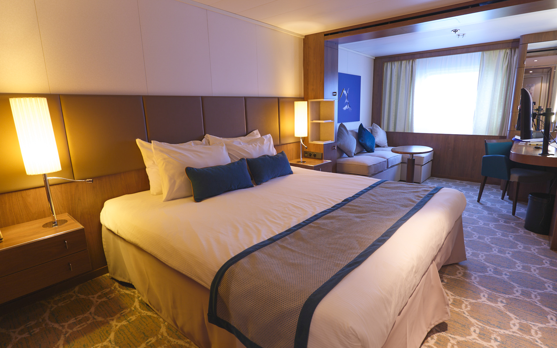 Deck 5 Superior cabin on Heritage Adventurer ship. King bed with white linens & brown bed runner. Tan couch & window beside it.