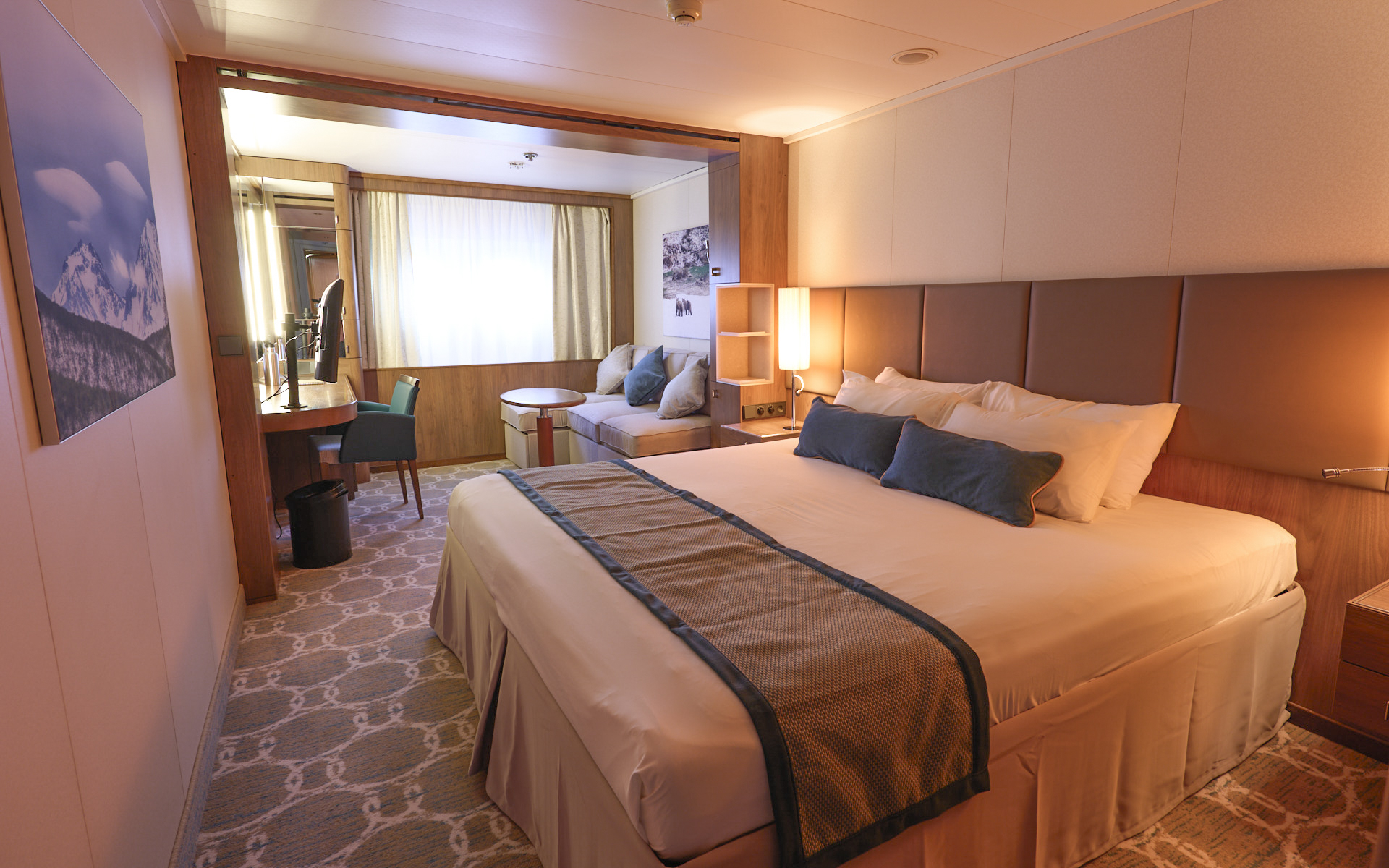 Main Deck Single cabin on Heritage Adventurer ship. King bed with white linens & brown bed runner. Tan couch & window beside it.