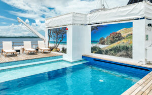 Rectangular teal outdoor pool with white chaise lounge chairs & colorful picture posters aboard the Heritage Adventurer ship.