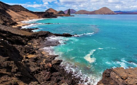 View from the top of hike on Bartolome island in the Galapagos, looking down on large rock formations that jet out from the teal ocean water.