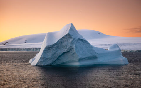 An iceberg floating in the ocean with a dramatic orange sky above during the Le Commandant Charcot Weddell Sea Voyage