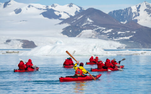 Kayakers in orange jackets paddle in the ocean near Pitt Point in Antarctica during the Le Commandant Charcot Weddell Sea Voyage.