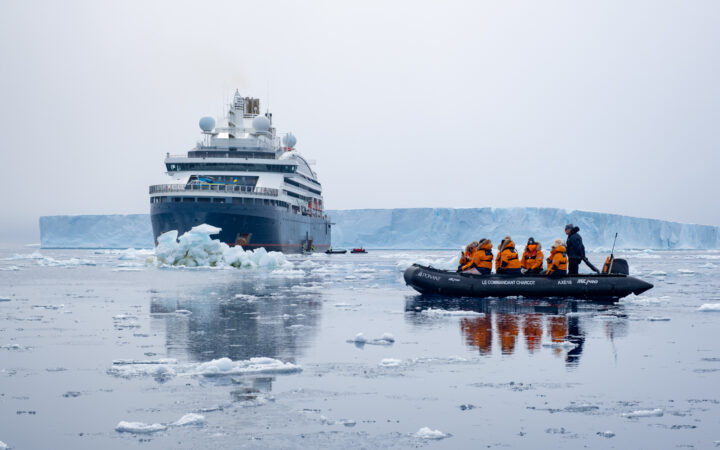 Passengers in orange jackets float in a zodiac amongst ice in the ocean during the Le Commandant Charcot Weddell Sea cruise.