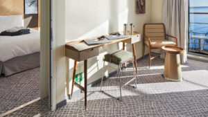 Corner of shared area with desk, cushioned stool & chair with side table overlooking balcony from Grande Suite on Magellan Explorer