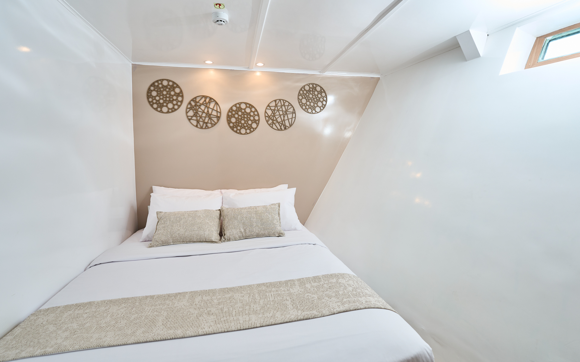 Lower Deck Cabin on Monserrat with matrimonial-size bed in white linens, beige accents & small, rectangular water-line window.