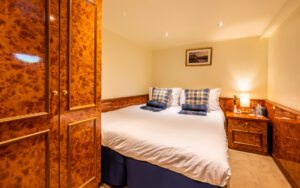 1 queen-sized bed with bedside table beside, 2 portholes, & walnut-wood large closet & desk aboard Spirit of Scotland hotel barge.