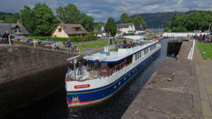 Spirit of Scotland hotel barge going through a Sottish loch in a small town on an overcast day.