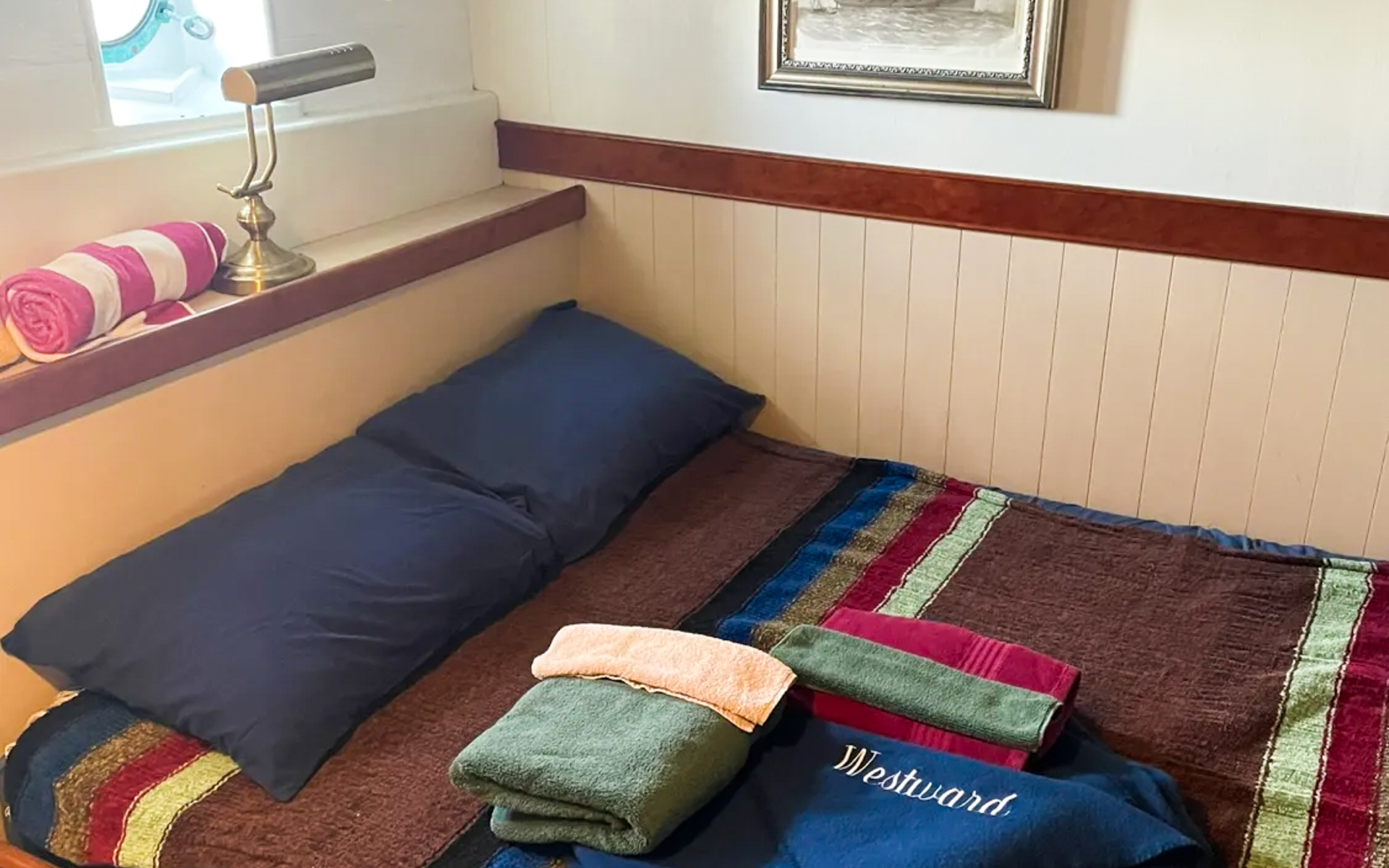 Cabin 2 aboard small ship Westward. Bed with brown, blue, red and green striped comforter. Dark blue pillows and towels displayed on bed.