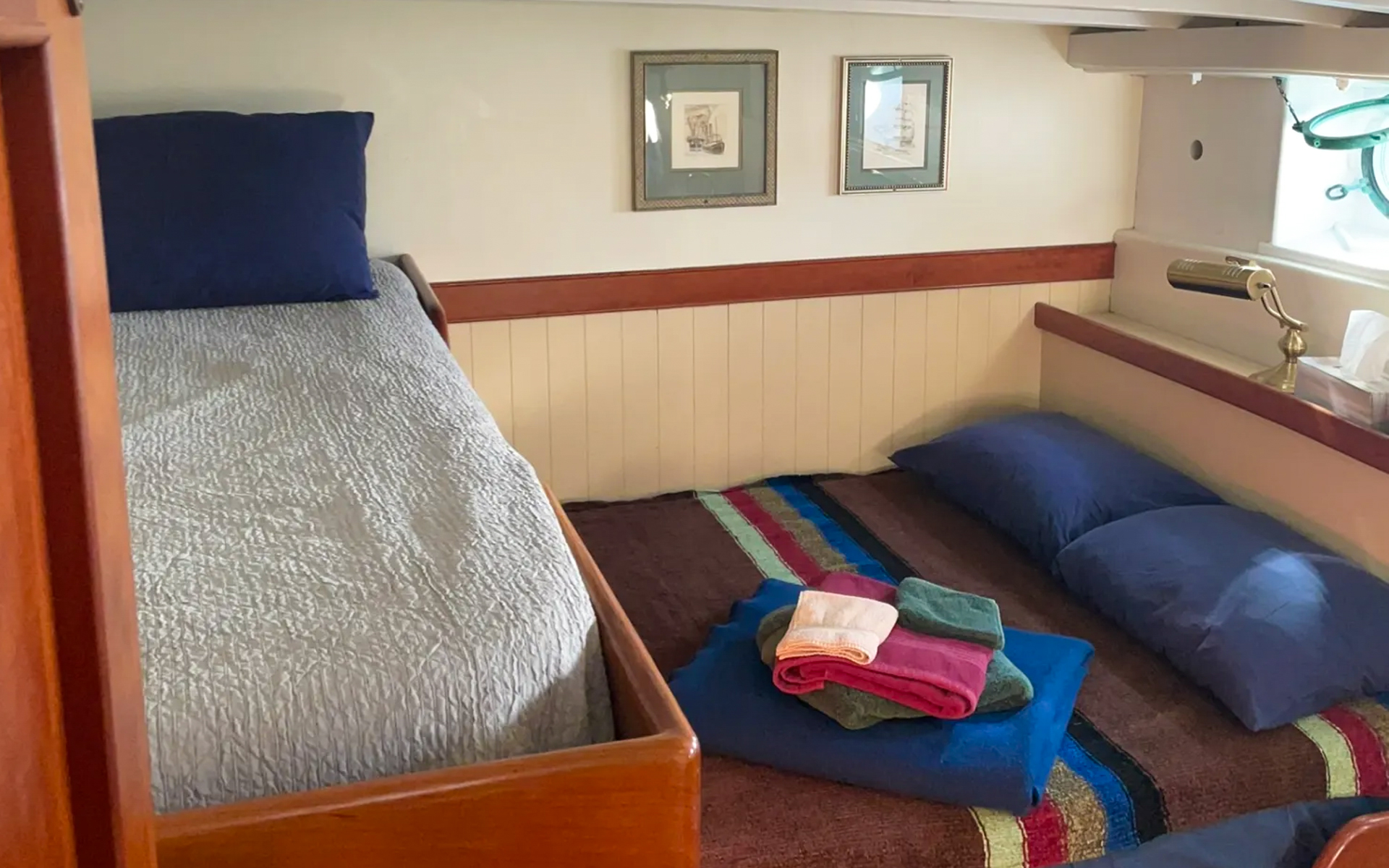 Cabin 4 aboard small ship Westward. Bunk beds with brown, blue, red and green striped comforter. Dark blue pillows and towels displayed on bed.
