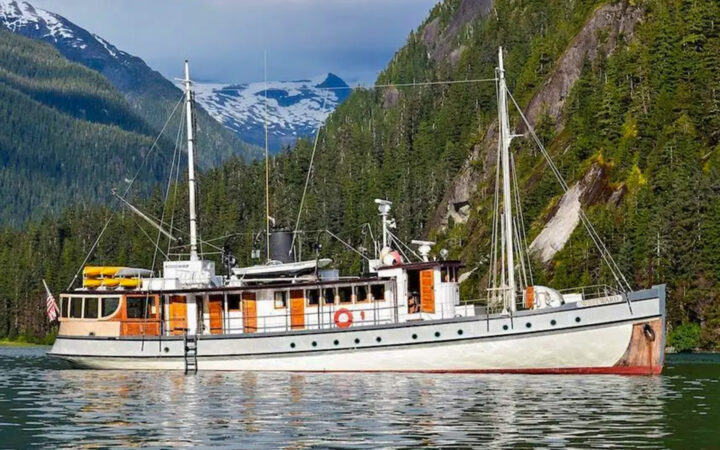 Exterior of Westward small cruise showing starboard side on a partly cloudy day with pine tree forest in background.