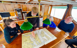 Captain bill and guests gather around table aboard westward yacht and look at map of inside passage Alaska to plan their route