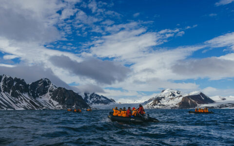 Five zodiacs with travelers in orange jackets head toward land in choppy arctic water during Spitsbergen Highlights small ship cruise