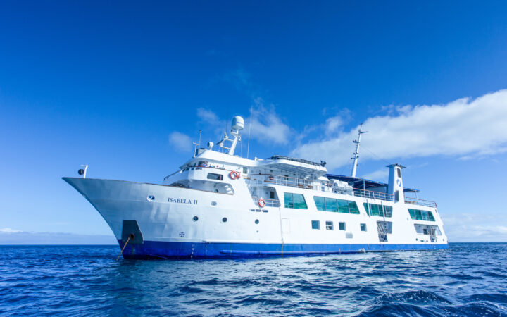 Exterior of Isabela II small ship's port side. White yacht with blue hull anchored under sunny blue skies in the Galapagos.