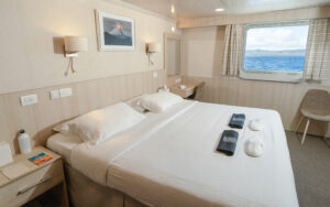 Small ship Isabela II Owners Cabin double bed with white linens, volcano photo over head, nightstand, window, small table and chairs.