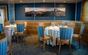 Dining room on Main Deck aboard small ship Isabela II with round tables and chairs set up for a meal and buffet service bar.