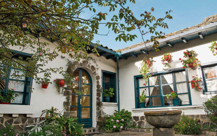 Spotless white walls and blue wooden pained windows of Hacienda Zuleta, seen from a floral-rich courtyard on a sunny day.
