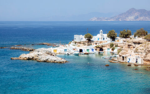 Fishing village in Mandrakia with colorful boat houses, bright blue ocean water, and boats during Greek Island small ship cruise