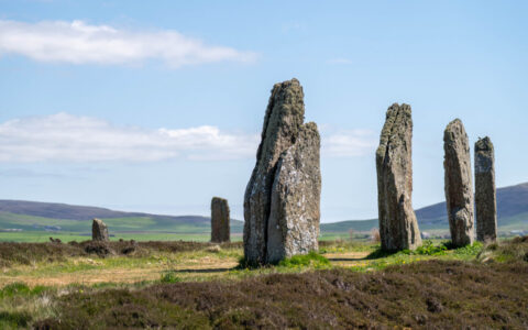 Tall, slender stones stand in a ring among green & gold grass, seen on the Isles of the North Atlantic Cruise in Scotland,