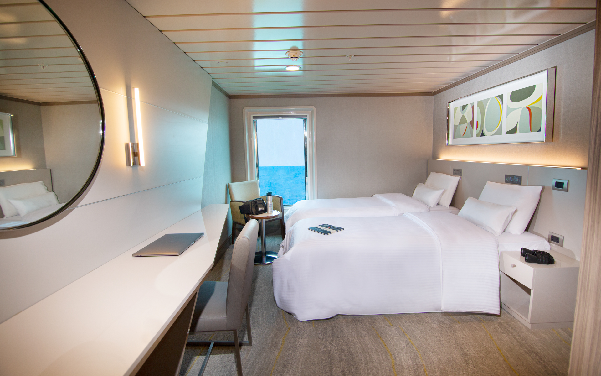 Luxury Twin Cabin aboard small ship La Pinta. Twin bed fitted with white linens, desk, mirror, armchair, nightstand & large window.