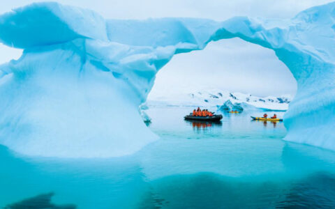 Kayaking and zodiac near an ice arch in the sea on the National Geographic Antarctica, South Georgia and The Falklands cruise