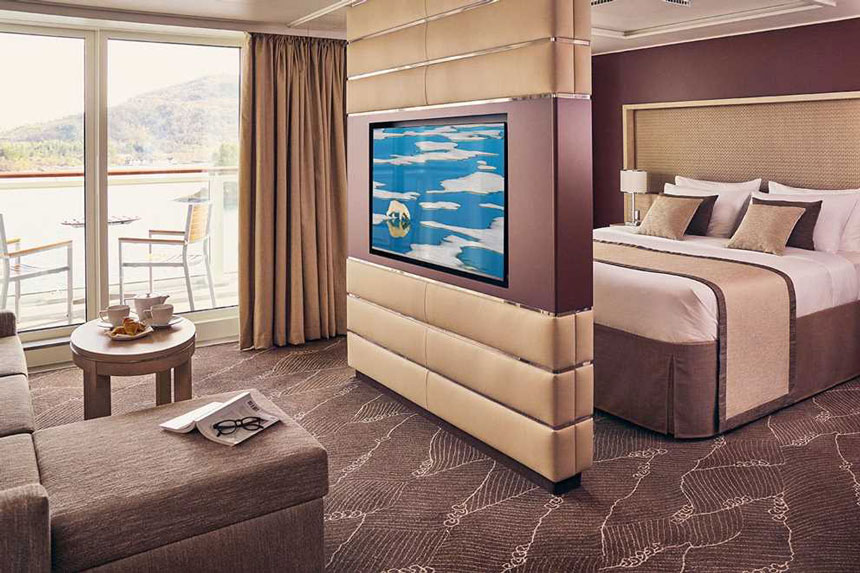 Balcony Suite with double bed, couch, desk, chair, and private balcony with table and chairs aboard National Geographic Endurance polar expedition ship.