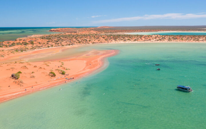 Aerial view of red sand bars with green scrub brush hosting travelers swimming on western Australia cruises.