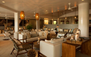 Lounge with cream-colored couches, wooden chairs, tables and abundant natural light at Finch Bay Eco Hotel in the Galapagos