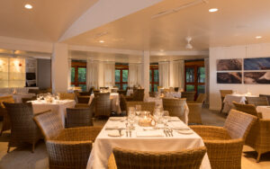 Dining room with 12 visible tables set for a meal, surrounded by large wicker chairs at Finch Bay Eco Hotel in the Galapagos