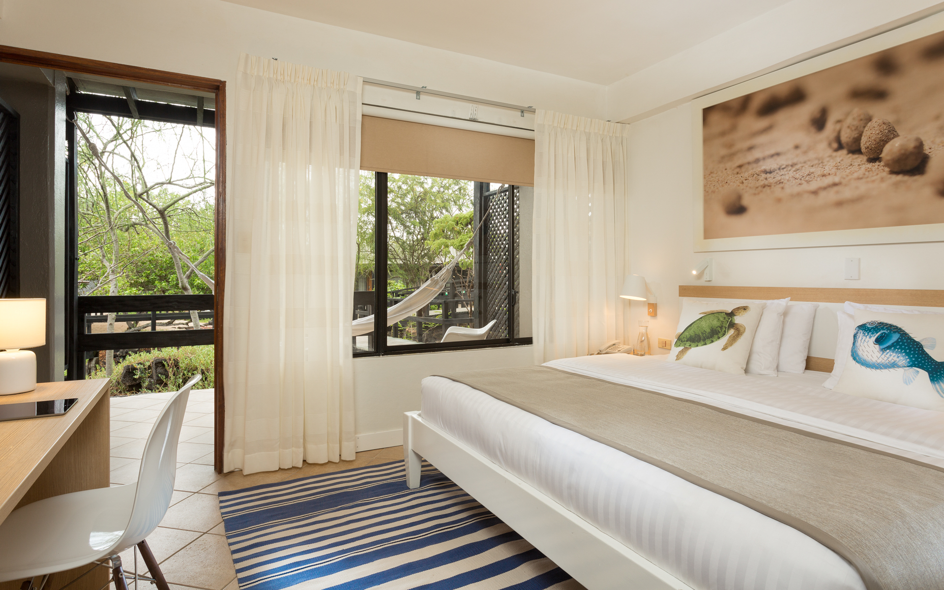 Finch Bay Eco Hotel "Finch Bay Room" with king bed and desk inside, hammock on patio with view of tree-dense area in the Galapagos Islands.