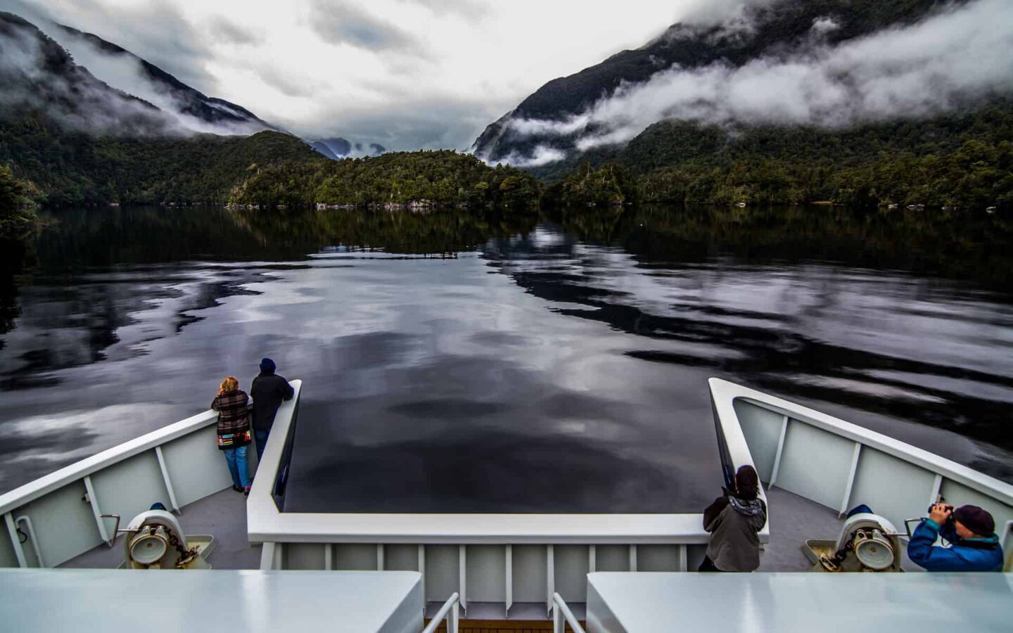 overlooking the bow of a luxury catamaran small ship in new zealand on calm water with mountains on either side