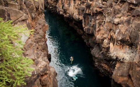 solo traveler on the galapagos discovery land tour in mid air between 2 cliffs above a narrow strip of water
