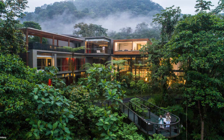 Exterior of Mashpi Lodge in Ecuador at dusk, with big glass windows and viewing platform surrounded by green vegetation and fog