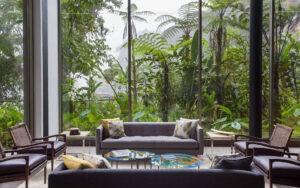 Lounge at Mashpi Lodge, with panoramic floor-to-ceiling windows, modern couches & coffee table with books on the surrounding wildlife.