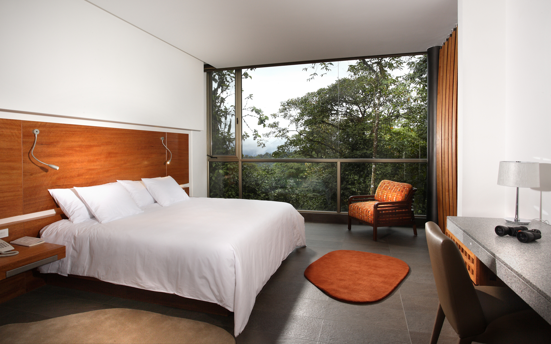 King-sized bed in Wayra Room next to orange armchair and and a private patio overlooking the jungle at the Mashpi Lodge in Ecuador.