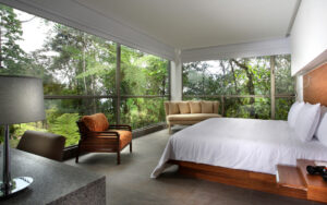 The Yaku King Suite with large bed, fresh white linens and massive windows providing a panoramic view of the jungle at Mashpi Lodge